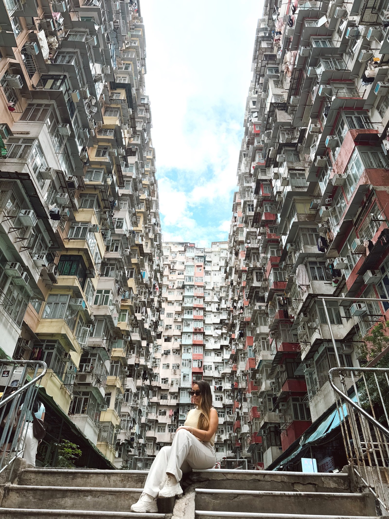 Denise sentada entre os prédios apertados de Hong Kong